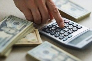 Close-up of man's hand using calculator and stacks of dollar bills
